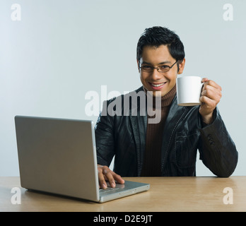 Man working on a laptop and drinking a cup of coffee Stock Photo