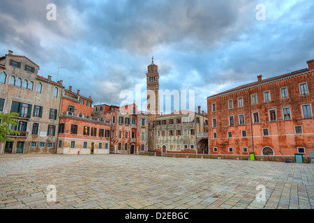 Small plaza among old typical colorful buildings and tall belfry on background under beautiful cloudy sky at evening in Venice. Stock Photo