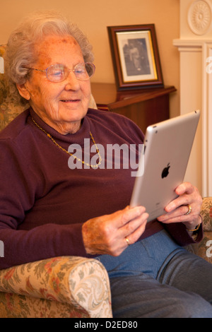 Elderly woman pensioner with glasses on apple ipad tablet at home relaxing on chair reading a book