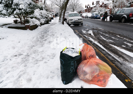 Rubbish awaiting collection at the side of a suburban road in the snow. Stock Photo