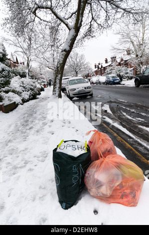 Rubbish awaiting collection at the side of a suburban road in the snow. Stock Photo