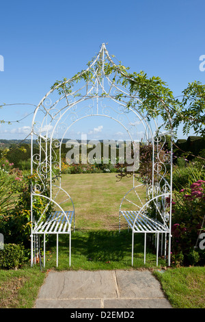White wrought-iron arbour and garden seats, in garden setting Stock Photo