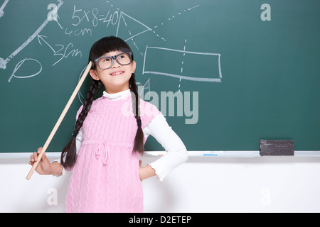 Humorous little girl playing teacher in classroom Stock Photo