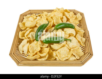 An old wicker basket filled with jalapeño seasoned potato chips with three fresh whole jalapeño peppers on top. Stock Photo