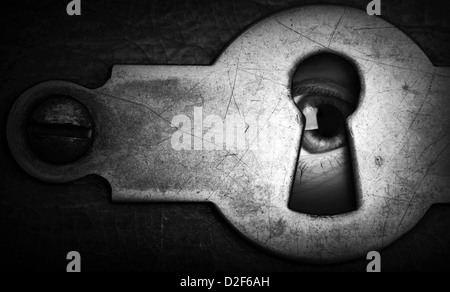 Eye looking through an old dark metal keyhole Stock Photo