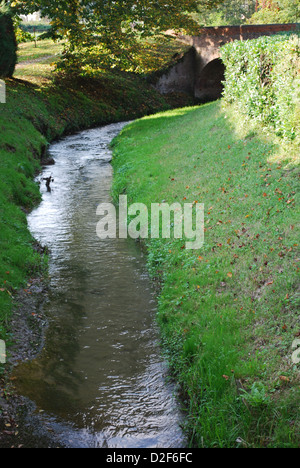 Narrow water river stream going through a green grass field Stock Photo