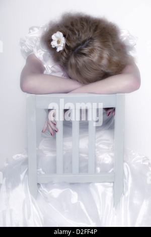 a woman in a white dress is sitting on a white chair and is crying Stock Photo