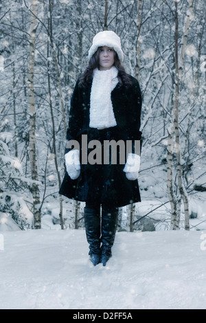 a woman in a black coat with a white hat and white scarf in the snow Stock Photo