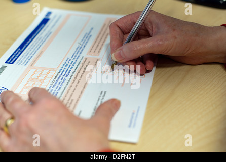 Older white woman's hand filling in an official form, tcking boxes and signing the paperwork Stock Photo