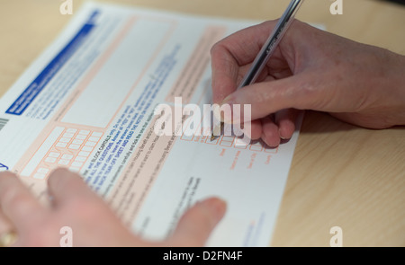 Older white woman's hand filling in an official form, tcking boxes and signing the paperwork Stock Photo