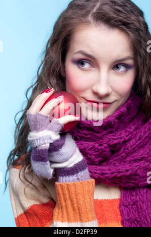 Young pretty woman in winter dress on blue background with Christmas ball in hands Stock Photo