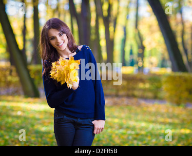 Portrait of smiling, young woman, holding a bunch of autumn maple leaves. Stock Photo