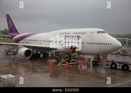 A Thai airways 747 jumbo being loaded at Phuket airport in heavy rain ...