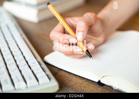 Hands writes a pen in a notebook, keyboard, a stack of books in background. Stock Photo