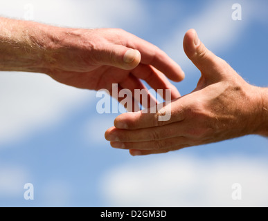 Two hands reaching out to each other against sky Stock Photo