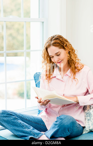 Smiling caucasian woman reading book by window at home Stock Photo