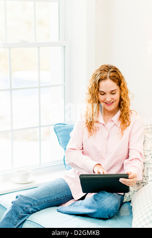 Smiling caucasian woman using tablet computer at home by window Stock Photo