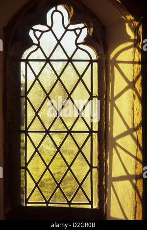 15th century Perpendicular Gothic diamond leaded window in warm early evening light casting shadows in niche Stock Photo