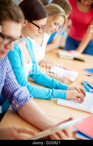 Portrait of pretty girl typing on laptop among her group mates Stock Photo