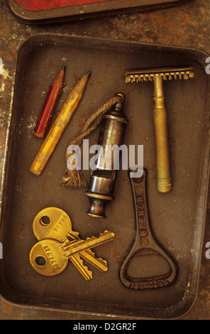 Small tin containing vintage razor whistle bottle-opener two door keys and two pencil stubs Stock Photo