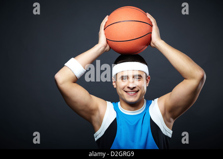 Portrait of handsome guy in sportswear with basket ball on his head looking at camera