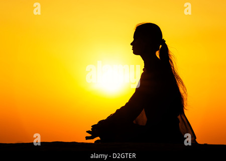 Sunset silhouette of an Indian girl meditating. Andhra Pradesh, India