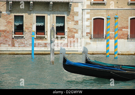 Detail view of Venice canal with a few colourful mooring posts and the front of two gondolas. A gull stands on one of the posts Stock Photo