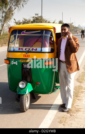 Successful rickshaw driver with new rickshaw using mobile phone. Model released Stock Photo