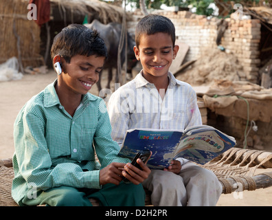 India, Agra, Child in school uniform using smartphone, wearing bluetooth headset and brother reading english textbook Stock Photo