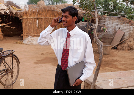 India,Uttar Pradesh, Agra, Young adult man wearing shirt and tie holding laptop using mobile outside village home Stock Photo