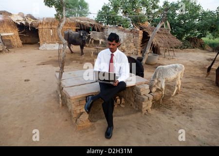 India,Uttar Pradesh, Agra, Young businessman in shirt and tie looking at laptop outside village home Stock Photo