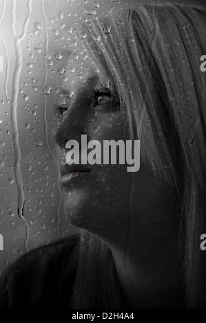 A female model taken through a window with rain drops running down the window pane. Stock Photo