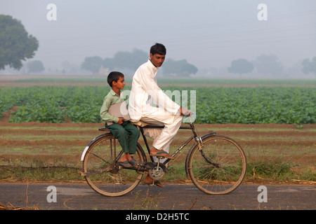 india, Uttar Pradesh, young male riding bike with younger boy in school uniform on carry rack holding laptop Stock Photo