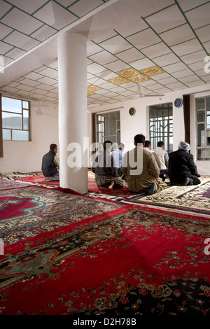 Muslim men in village mosque at prayer kneeling on red carpet In Kurdistan, North Iraq Stock Photo