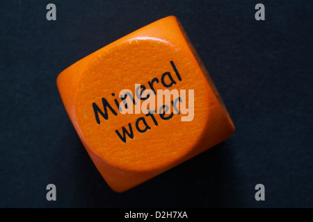throw of an orange coloured drinking dice showing Mineral Water isolated on black background Stock Photo