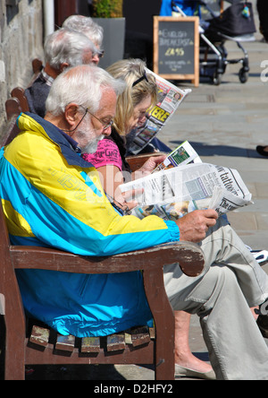 middle aged man sitting on bench reading newspaper, Whitby, North Yorkshire, England, UK Stock Photo