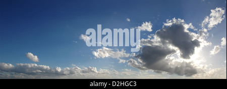 Blue sky with several cumulus clouds in background and a large cloud masking the sun, in the foreground generating some god rays Stock Photo