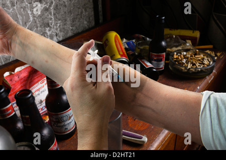 Heroin drug user injects his arm using a hypodermic syringe in a dirty bedroom (B&W - see D2HT21 for colour alternative)