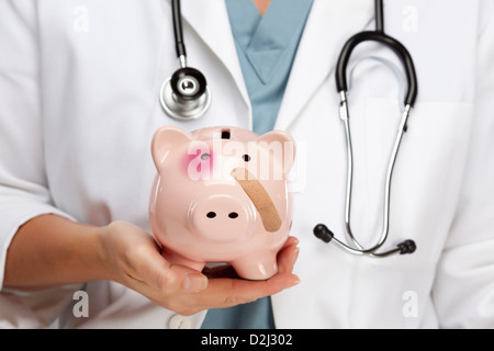 Female Doctor with Stethoscope Holding Piggy Bank with Bruised Eye and Bandage. Stock Photo