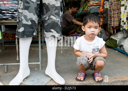 Bangkok, Thailand, a small boy sits in front of the textile shop of the father Stock Photo