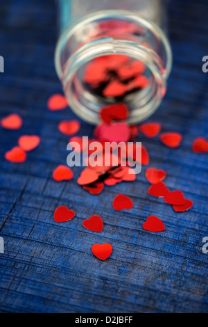Shiny red love hearts coming out of a glass jar on blue wood background Stock Photo