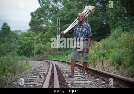 Stock photograph of a black South African entrepreneur small business broom salesman on railway line in Hilton. Stock Photo