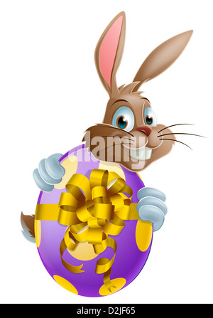 Cute Easter bunny cartoon character holding onto and peeking round a painted chocolate Easter egg Stock Photo
