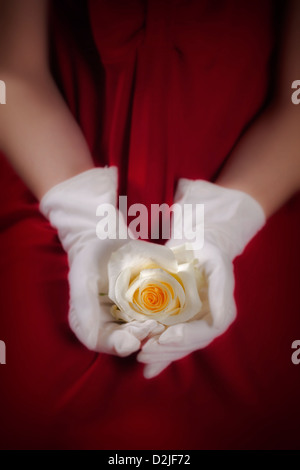 a woman in a red dress with white gloves is holding a white rose on her lap