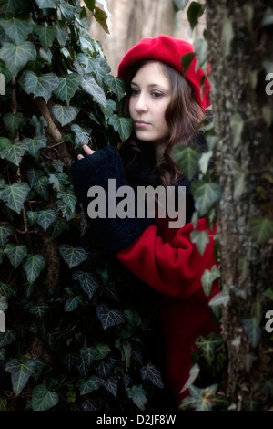 a woman with a red coat and hat between two trunks Stock Photo