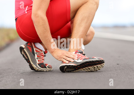 Low section of young male runner touching foot in pain due to sprained ankle on road Stock Photo