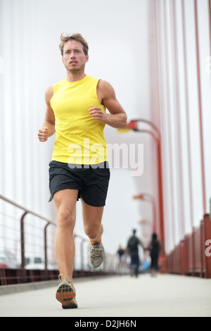 Fit runner running outside. Young male fitness model training in yellow on Golden Gate Bridge, San Francisco, California, USA Stock Photo