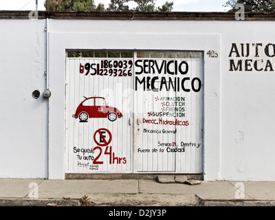 charming red & black sign hand painted on white gate in plaster wall advertising 24 hour auto mechanic service Oaxaca Mexico Stock Photo