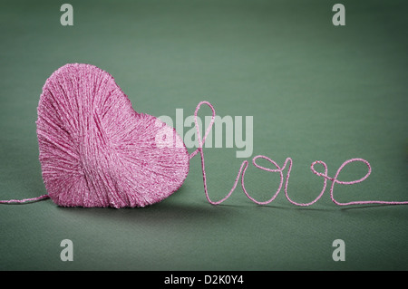Pink clew in shape of heart with word 'love' made from yarn on green background Stock Photo