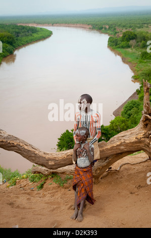 Portrait of Kara boy and child sitting on log-Omo River below Stock Photo